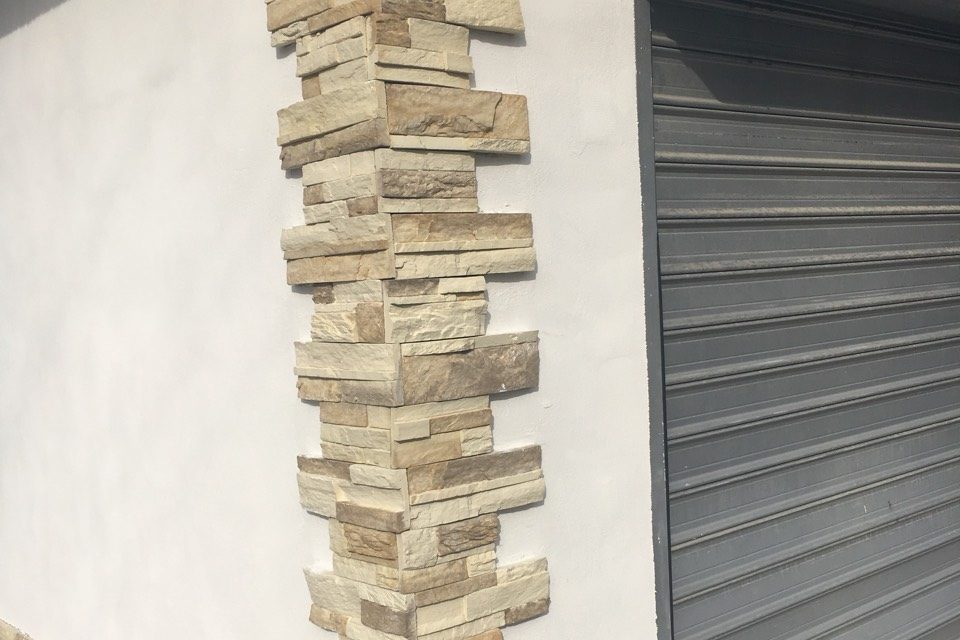 Mason installing cast stone veneer on a house wall